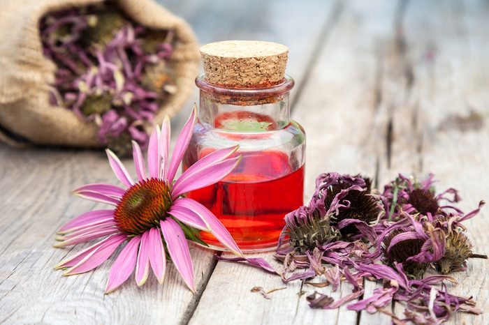 essential oil in glass bottle and coneflower on wooden rustic table, bag with herbs, herbal medicine