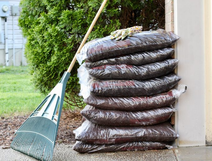 Close up view of stacked plastic bags of commercial organic mulch and a rake from a nursery for garden maintenance in spring